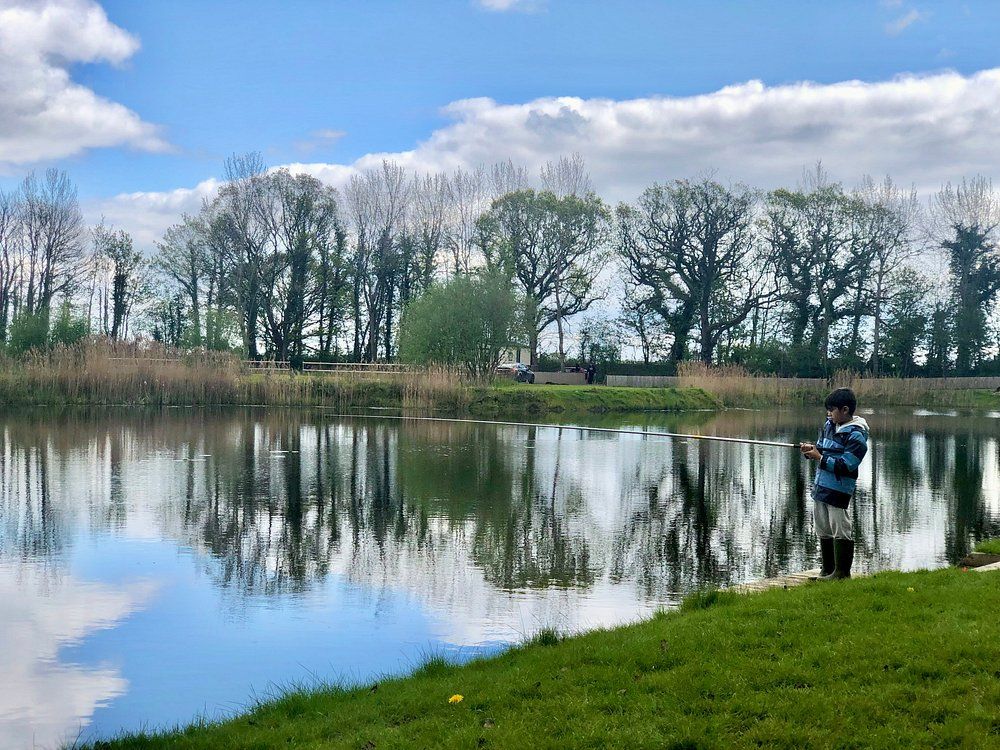 Angler fishing at Willow Garth lake with peaceful woodland backdrop and reflective water